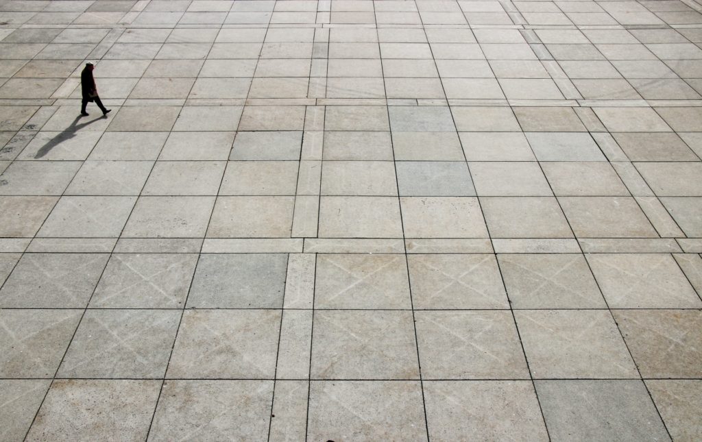 Person walking into a vast space, made of large pavement tiles